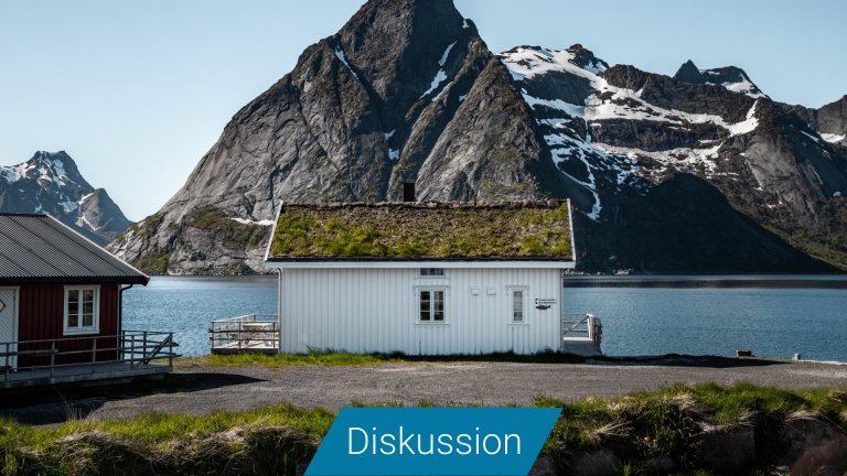 Ein weißes Holzhaus mit begrüntem Dach vor einem Fjord.